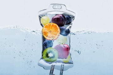 A conceptual graphic of an IV bag filled with fresh fruit slices floating in blue water, representing nutrient-rich vitamin therapy