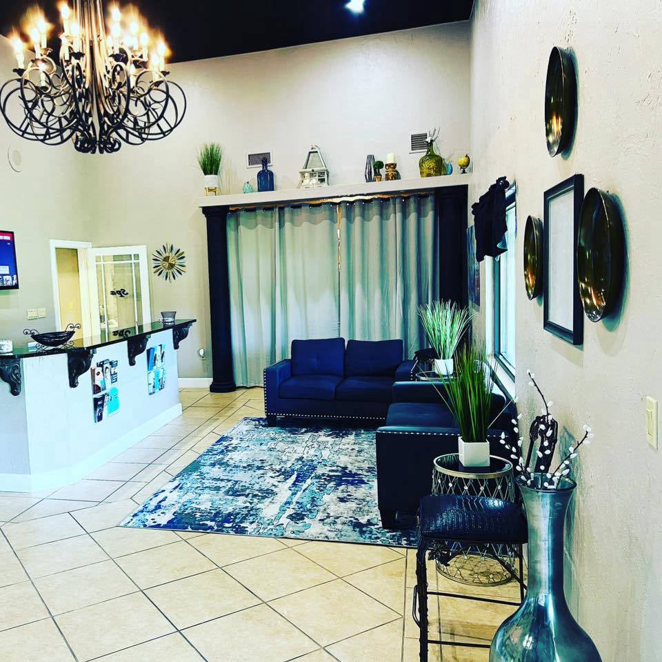 Interior of True Aesthetics & Wellness showing the front desk and client waiting area Bright, modern spa reception area featuring a front desk, navy seating, patterned rug, chandelier, and decorative wall accents