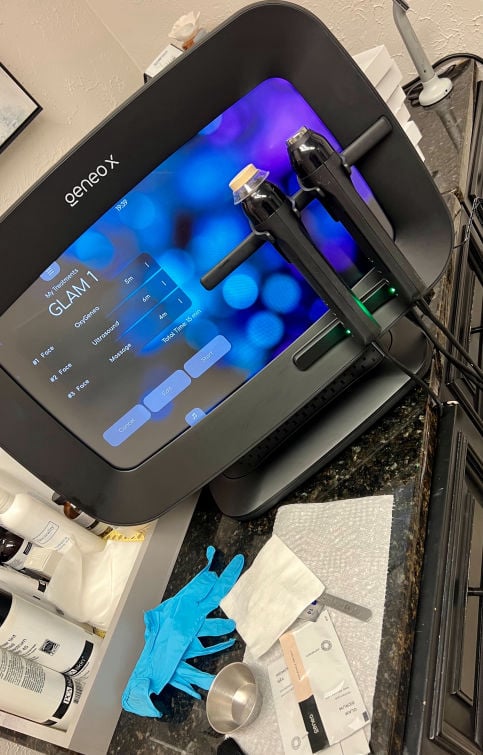 A Geneo X aesthetic platform with a digital touchscreen showing 'GLAM 1' treatment settings and two handheld applicators