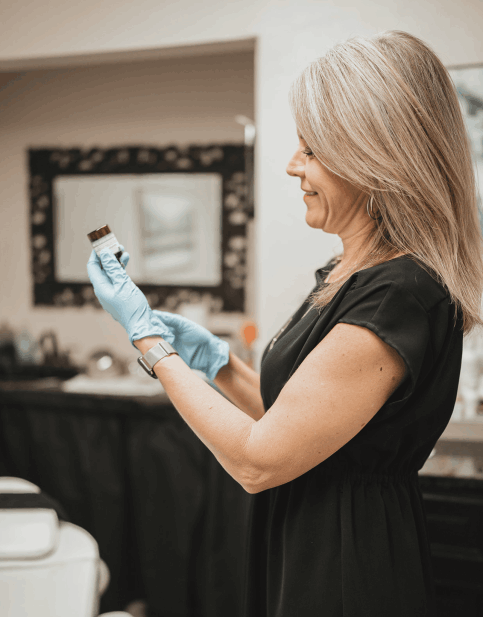 A professional in blue gloves inspecting a small medical vial of B-12 solution in a clinical setting