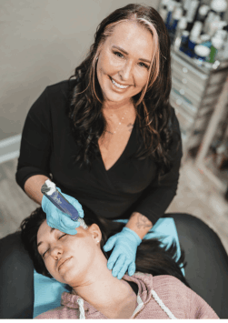 Professional in a black top and light blue gloves uses a blue SkinPen microneedling device to perform a facial treatment on a client lying down